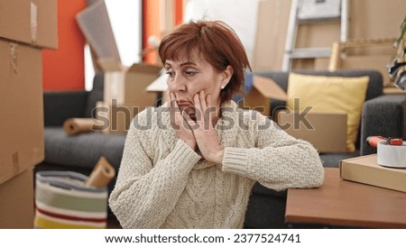 Mature hispanic woman sitting on the floor looking around tired at new home