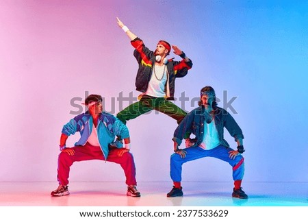 Team. Friends, tree men in colorful retro sportswear standing in pyramid pose against gradient pink blue background in neon light. Concept of sportive and active lifestyle, humor, retro style. Ad