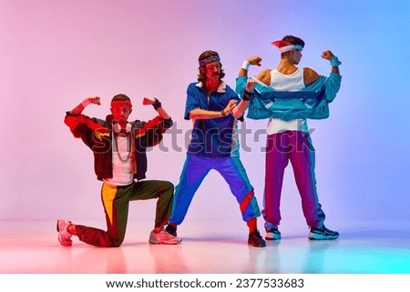 Showing muscles. Young men, fiends in colorful sportswear training against gradient pink blue background in neon light. Concept of sportive and active lifestyle, humor, retro style. Ad