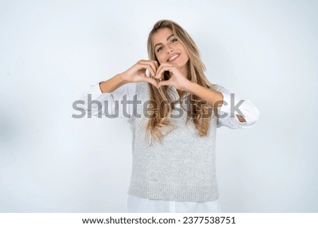 Beautiful hispanic blonde businesswoman smiling in love doing heart symbol shape with hands. Romantic concept.