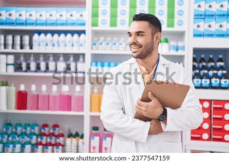 Young hispanic man pharmacist smiling confident holding clipboard at pharmacy