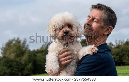 National pet day. A man hugs his Bichon Frise dog in the park. Happy man and dog love and friendship concept. 