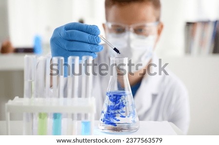 A male chemist holds test tube of glass in his hand overflows a liquid solution of potassium permanganate. Conducts an analysis of water samples versions of reagents using chemical manufacturing. Royalty-Free Stock Photo #2377563579