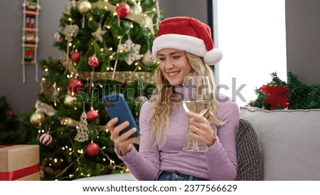 Young blonde woman celebrating christmas using smartphone drinking wine at home