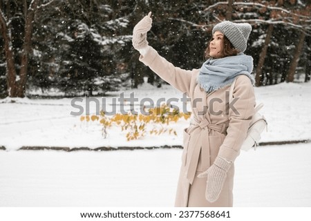 Cute girl takes a selfie in mittens under the snow with a backpack and a hat