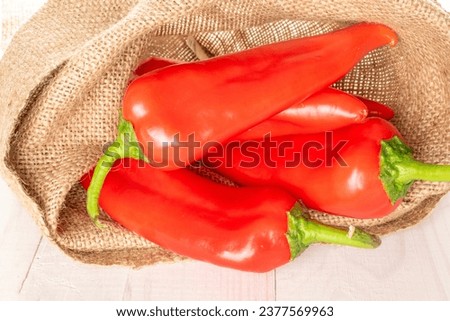 Three red sweet peppers with a jute bag on a wooden table