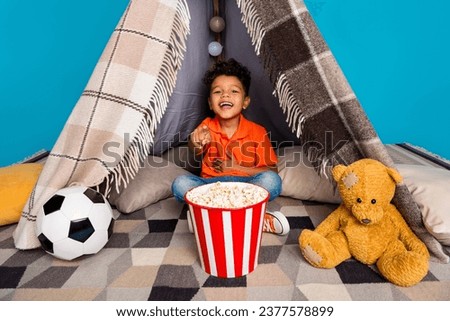Photo of funny cute boy watching comedy in playroom diy tent isolated over blue color background