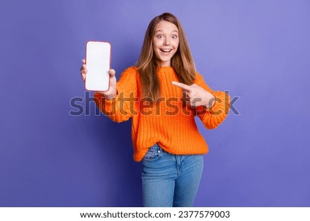 Photo of amazed cute teenager girl brown hair indicating finger copyspace in phone to put advert isolated on violet color background