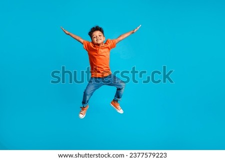 Full body cadre of jumping energetic latin small kindergarten age boy hands up positive star symbol hands isolated on blue color background Royalty-Free Stock Photo #2377579223