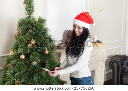 Young smiling woman in Santa hat decorating Christmas tree.