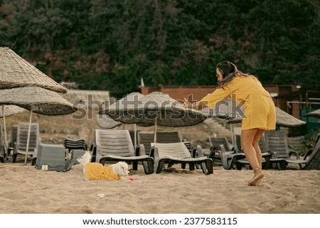 Woman in yellow dress is having a good time playing with her white Maltese dog in yellow dress on the beach