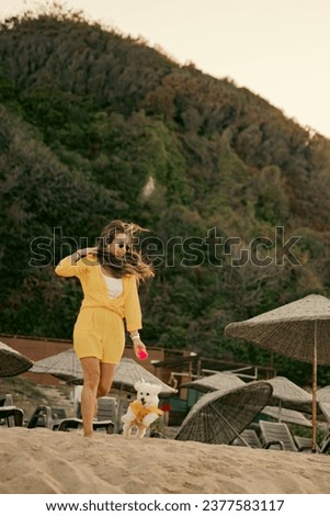 Woman in yellow dress is having a good time playing with her white Maltese dog in yellow dress on the beach