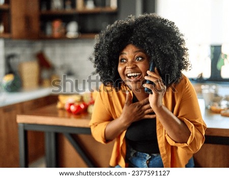 Happy young afro american woman having fun preparing food and a mobile phone in kitchen, or a young businesswoman working from home office making connections online, talking making a phone call Royalty-Free Stock Photo #2377591127