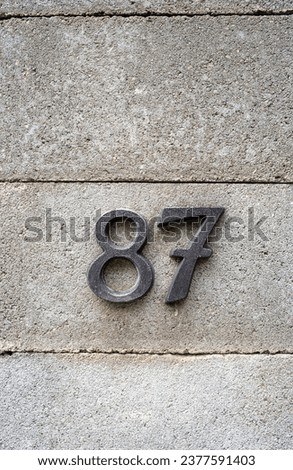 House number numerals on a concrete wall. Number 87 decorative types, close up, no people