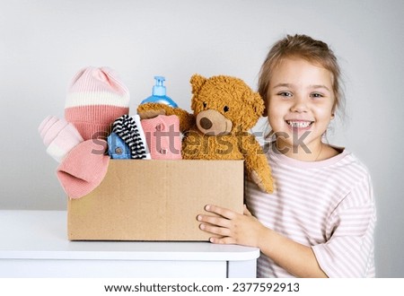 Caucasian child girl holding donation box with kid's stuff: clothes, toys, warm clothing. Donate concept. Little volunteer.