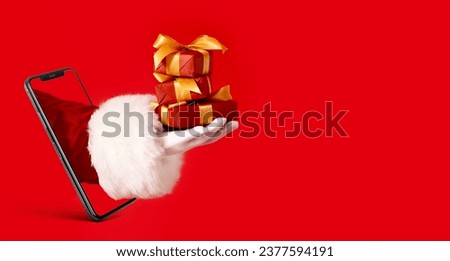 Mobile phone and hand of Santa Claus with Christmas gifts on red background with space for text Royalty-Free Stock Photo #2377594191