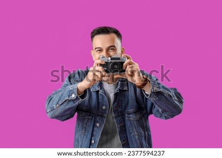 Happy young man with photo camera on purple background