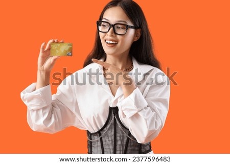 Young Asian woman pointing at credit card on orange background