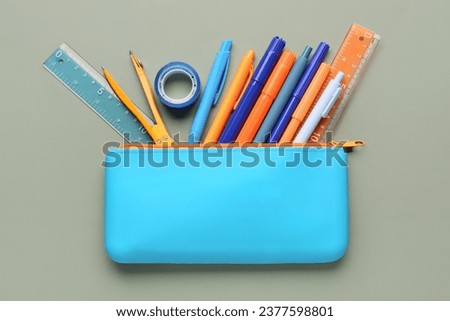 Blue pencil case with school stationery on green background Royalty-Free Stock Photo #2377598801