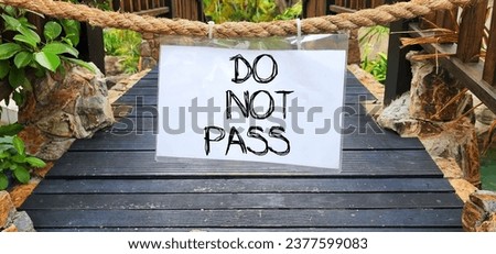 Do not pass sign hanging with a rope on a wooden bridge. The "Do not pass" in sign black message on a white paper sign hangs on hemp rope to block the area from unauthorized access. 