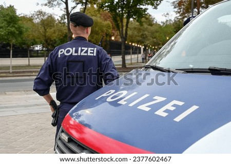 Policeman by police car. Policeman in uniform patrolling on the street. Police symbol on vehicle and uniform.