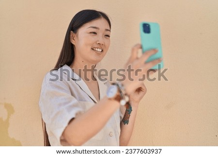 Chinese woman smiling confident making selfie by the smartphone over white isolated background