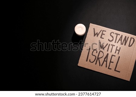 Text WE STAND WITH ISRAEL and burning candle on dark background