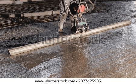 Workers uses vibrating machine to level cement mortar for floors. Concrete screed for buildings, construction site. Royalty-Free Stock Photo #2377625935