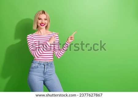 Portrait of optimistic cute girl with short hair wear stylish clothes indicating at empty space poster isolated on green color background