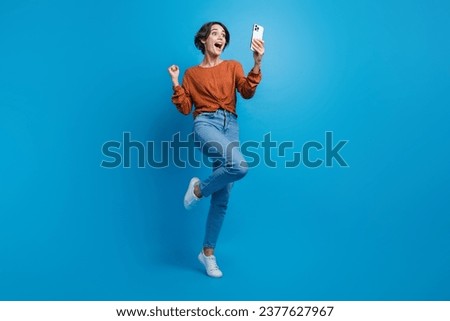 Full length photo of lovely young lady celebrate big discount eshop hold device wear trendy brown garment isolated on blue color background
