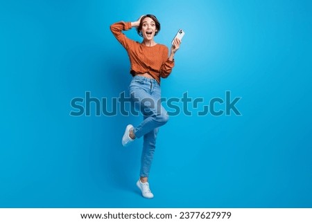 Full body photo of pretty young girl hold telephone amazed sales hold device wear trendy brown outfit isolated on blue color background