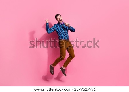 Full length photo of funky guy jumping high holding microphone singing his favorite song for girlfriend isolated on pink color background