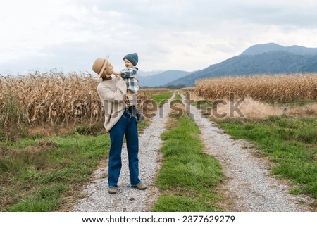 Mother and son walking playing together in agricultural field area. Happy woman with child on road in nature. Family traditions. Concept sustainable lifestyle, family bonding, natural parenting.