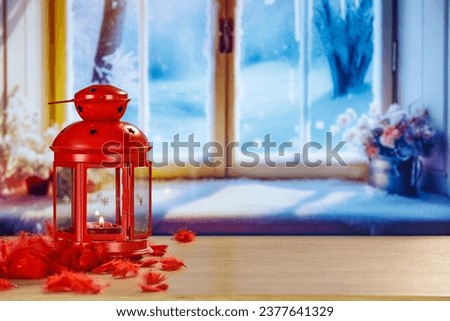 Red lamp with small candle on wooden desk and home interior background with big winter window. Sunny cold december day and natural light from window. Empty place for your products on mockup. 