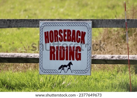 A sign attached to a wooden fence that says "Horseback Riding".