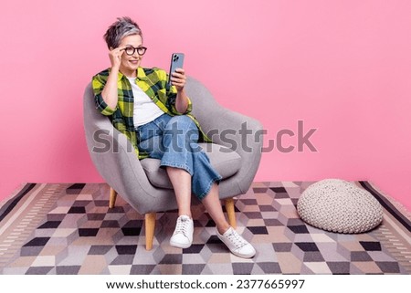 Full size photo of smart person dressed shirt sit on armchair touch glasses read email on smartphone isolated on pink color background