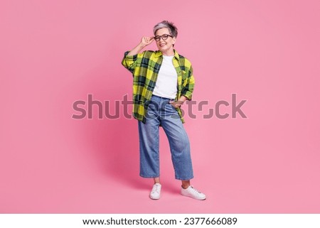 Full length photo of optimistic elderly woman wear checkered shirt touch eyewear hold hand in pocket isolated on pink color background