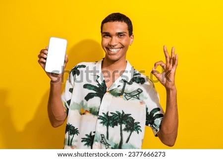 Photo of clever satisfied man with nose piercing demonstrate smartphone display empty space show okey isolated on yellow color background