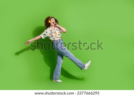 Full length photo of dreamy sweet lady wear print shirt singing enjoying songs earphones walking empty space isolated green color background
