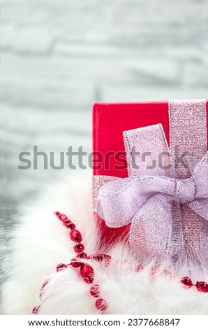 Gift box with silver bow in fluffy bag with red shiny beads on white background. Decorations. Christmas, New Year, birthday, holiday. Vertical. Copy space