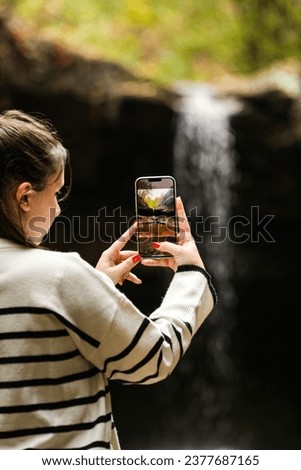 A very beautiful autumn landscape with a waterfall in the background where a young lady uploads to take a qualitative picture of this beautiful autumn landscape.