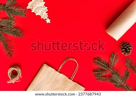 Christmas and new year festive Flat lay mock up gifts making, preparation and wrapping in kraft paper package on red background. Christmas tree branches, kraft package, cone, scissors and twine.