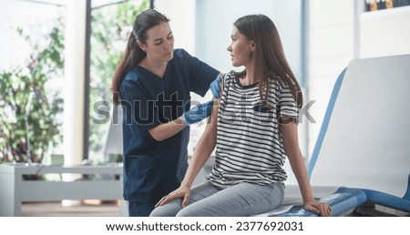 Happy Caucasian Woman Sitting In The Chair In Bright Hospital And Getting Her MMR Vaccine. Professional Female Nurse Is Performing Injection And Putting A Patch On. Public Healthcare Concept. Royalty-Free Stock Photo #2377692031