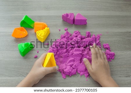 Little girl playing with bright kinetic sand at table indoors, closeup. Royalty-Free Stock Photo #2377700105