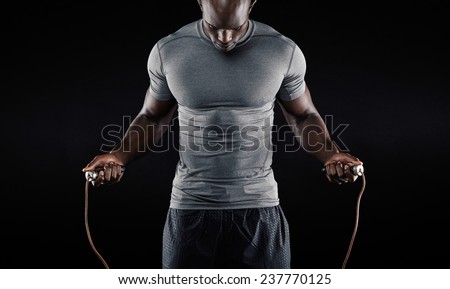Muscular man skipping rope. Portrait of muscular young man exercising with jumping rope on black background Royalty-Free Stock Photo #237770125