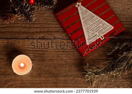 Christmas gift box and a lit candle with some Christmas tree branches on wooden background with copy space