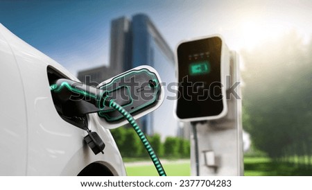 Electric car plug in with charging station to recharge battery with electricity by EV charger cable in eco green city park. Future innovative EV car using alternative clean energy reducing CO2. Peruse Royalty-Free Stock Photo #2377704283