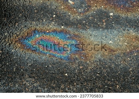 Spots of oil or gasoline are scattered randomly on the asphalt after rain. Abstract background close-up