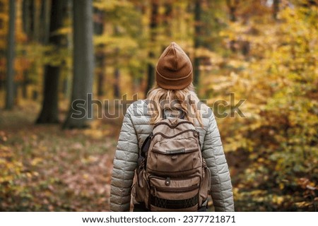 Woman with backpack hiking on footpath in autumn forest. Solo female tourist outdoors Royalty-Free Stock Photo #2377721871