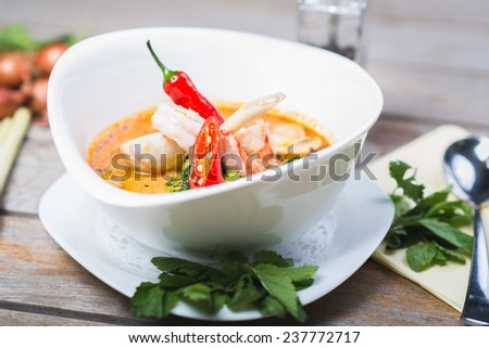 traditional spicy Thai Tom Yam soup on a wooden table with vegetables and herbs